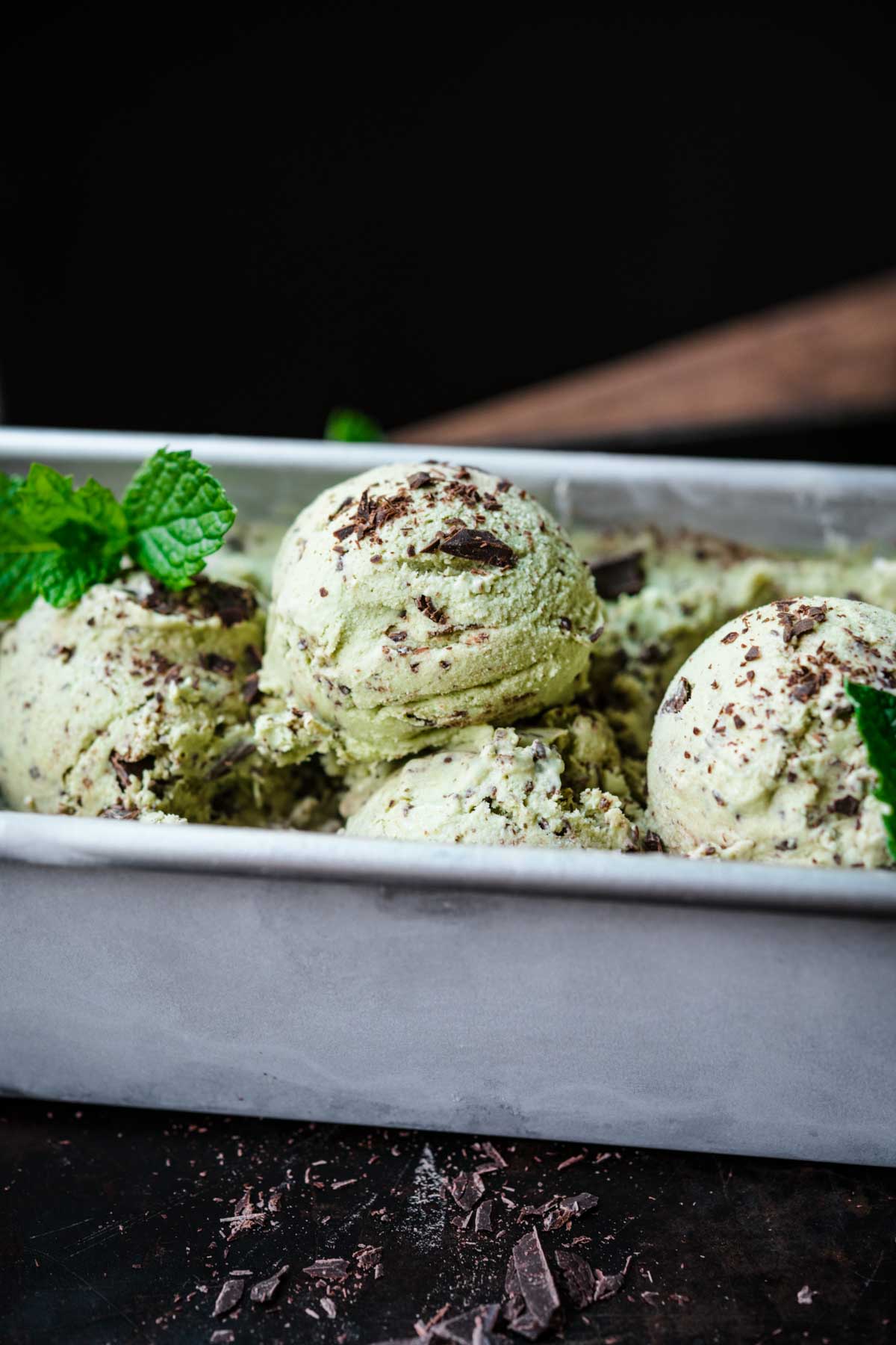 close up view of several scoops of vegan mint chocolate chip ice cream in metal tin. 