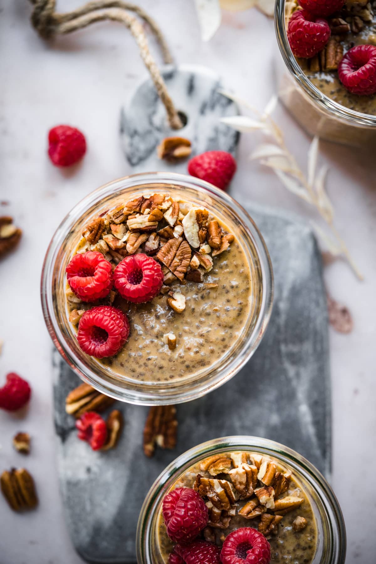 overhead view of vegan pumpkin chia pudding in small jars topped with pecans and raspberries. 