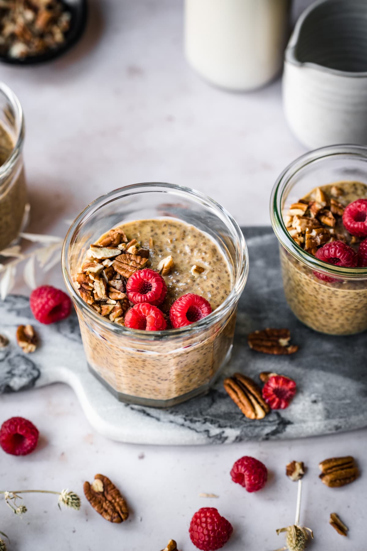 close up view of vegan pumpkin chia pudding in small jars topped with pecans and raspberries. 