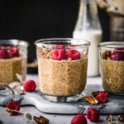 close up view of vegan pumpkin chia pudding in small jars topped with pecans and raspberries.