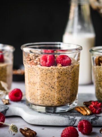 close up view of vegan pumpkin chia pudding in small jars topped with pecans and raspberries.