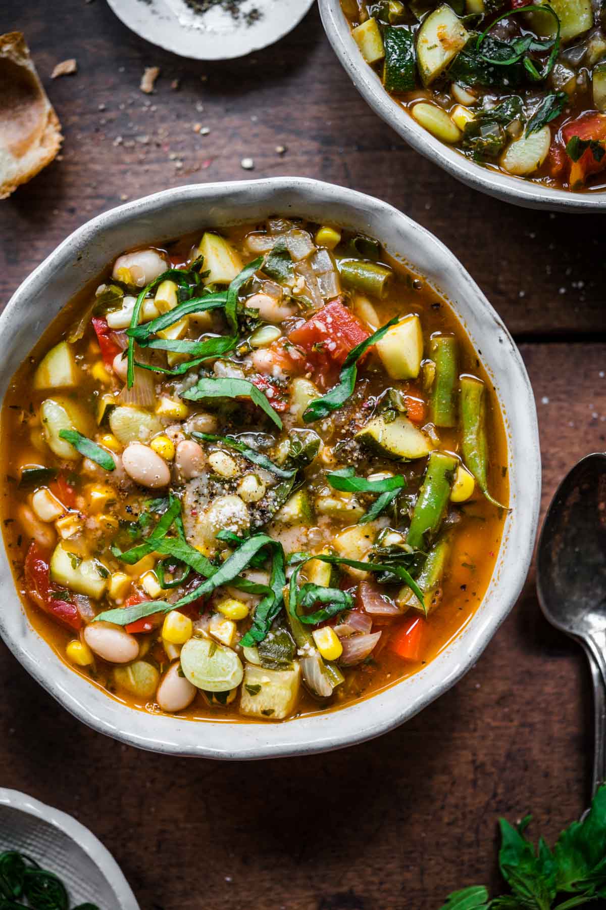 close up overhead view of summer minestrone soup in bowl with fresh basil on top.