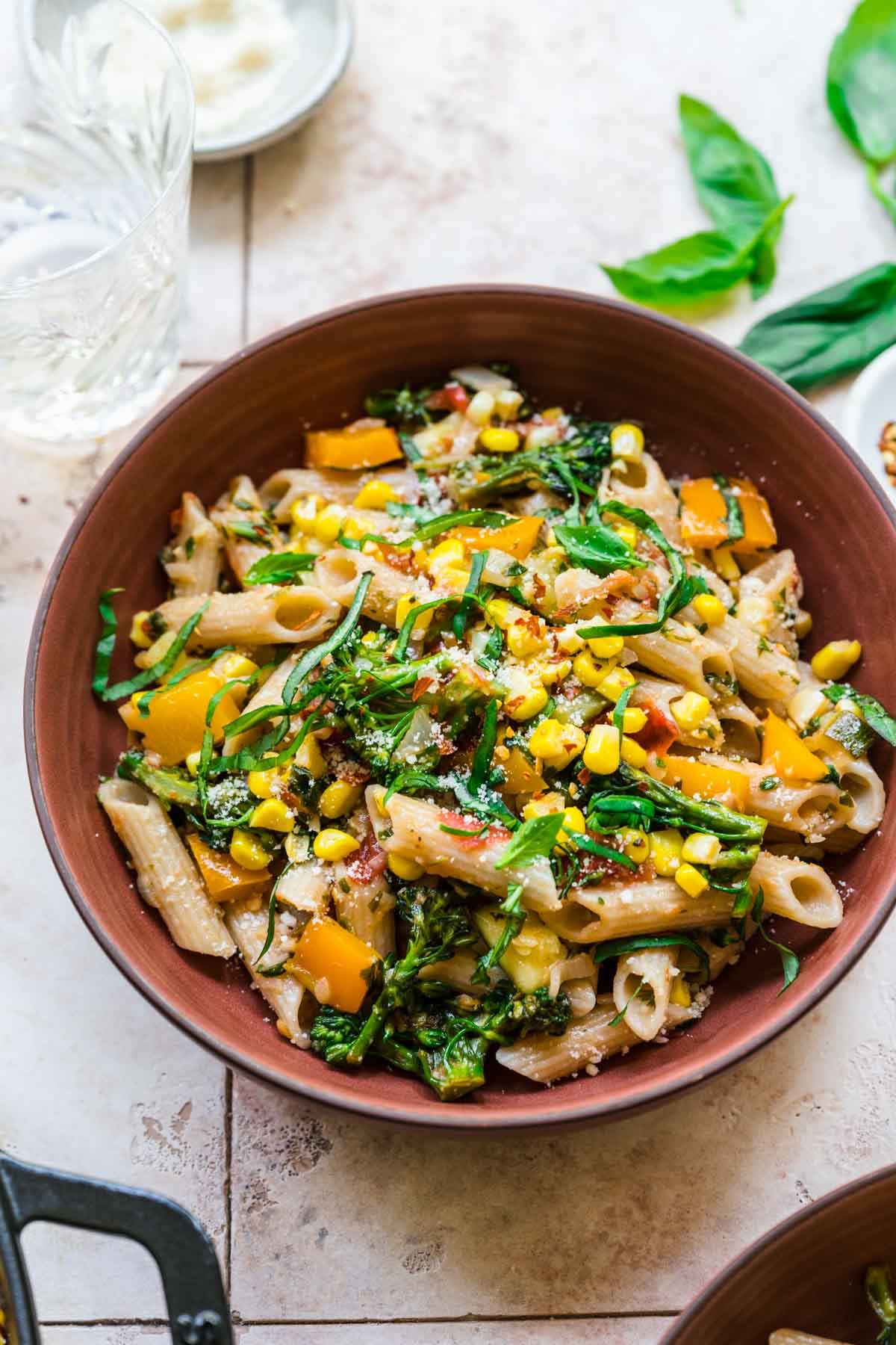 close up view of vegan pasta with summer vegetables in a red bowl. 