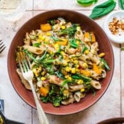 close up view of vegan pasta with summer vegetables in a red bowl.