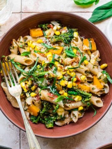 close up view of vegan pasta with summer vegetables in a red bowl.