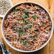 overhead view of large bowl of vegan coleslaw with serving spoon on wood table.