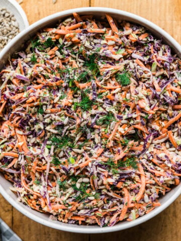 overhead view of large bowl of vegan coleslaw with serving spoon on wood table.