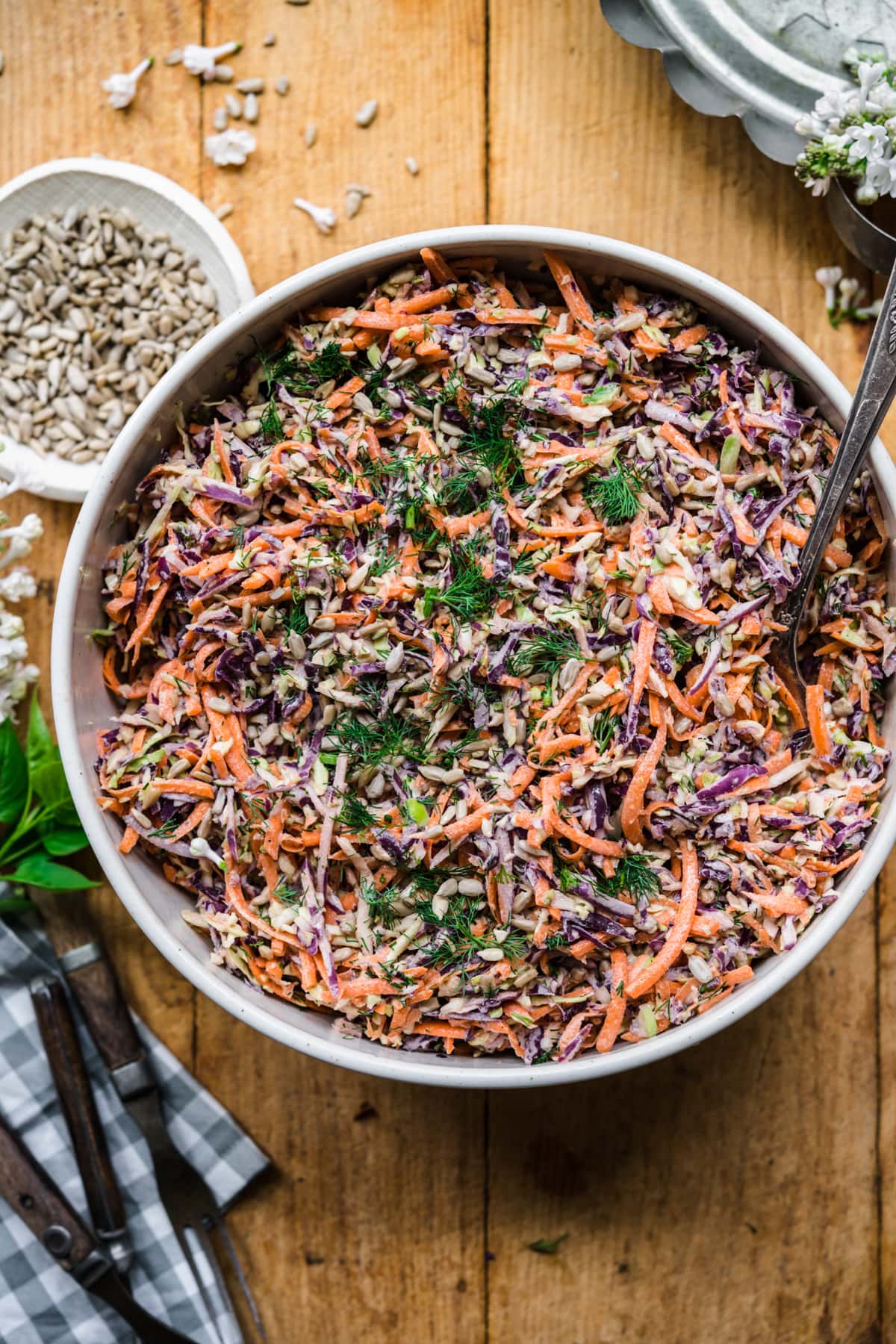 overhead view of large bowl of vegan coleslaw with serving spoon on wood table. 