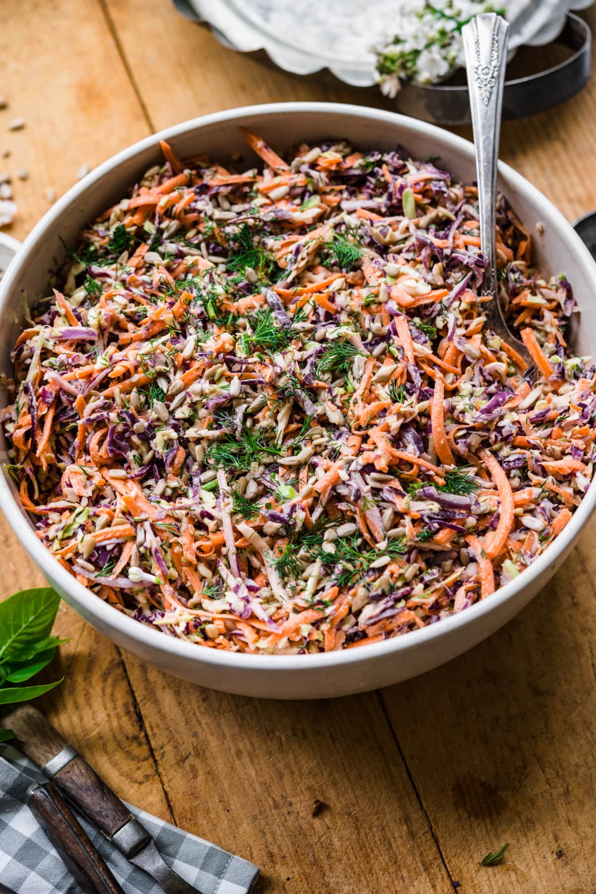 close up view of large bowl of vegan coleslaw with serving spoon on wood table. 