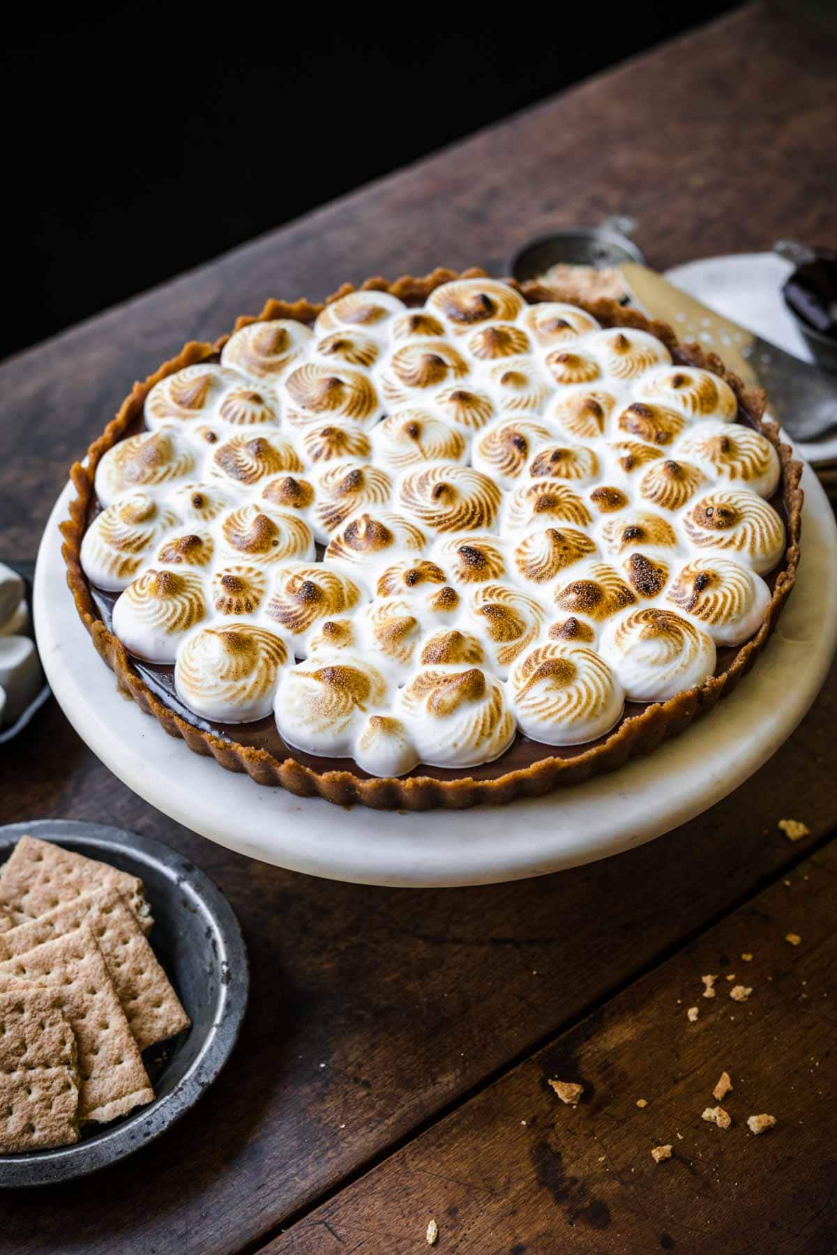 side view of full vegan meringue tart on cake stand on wood table. 