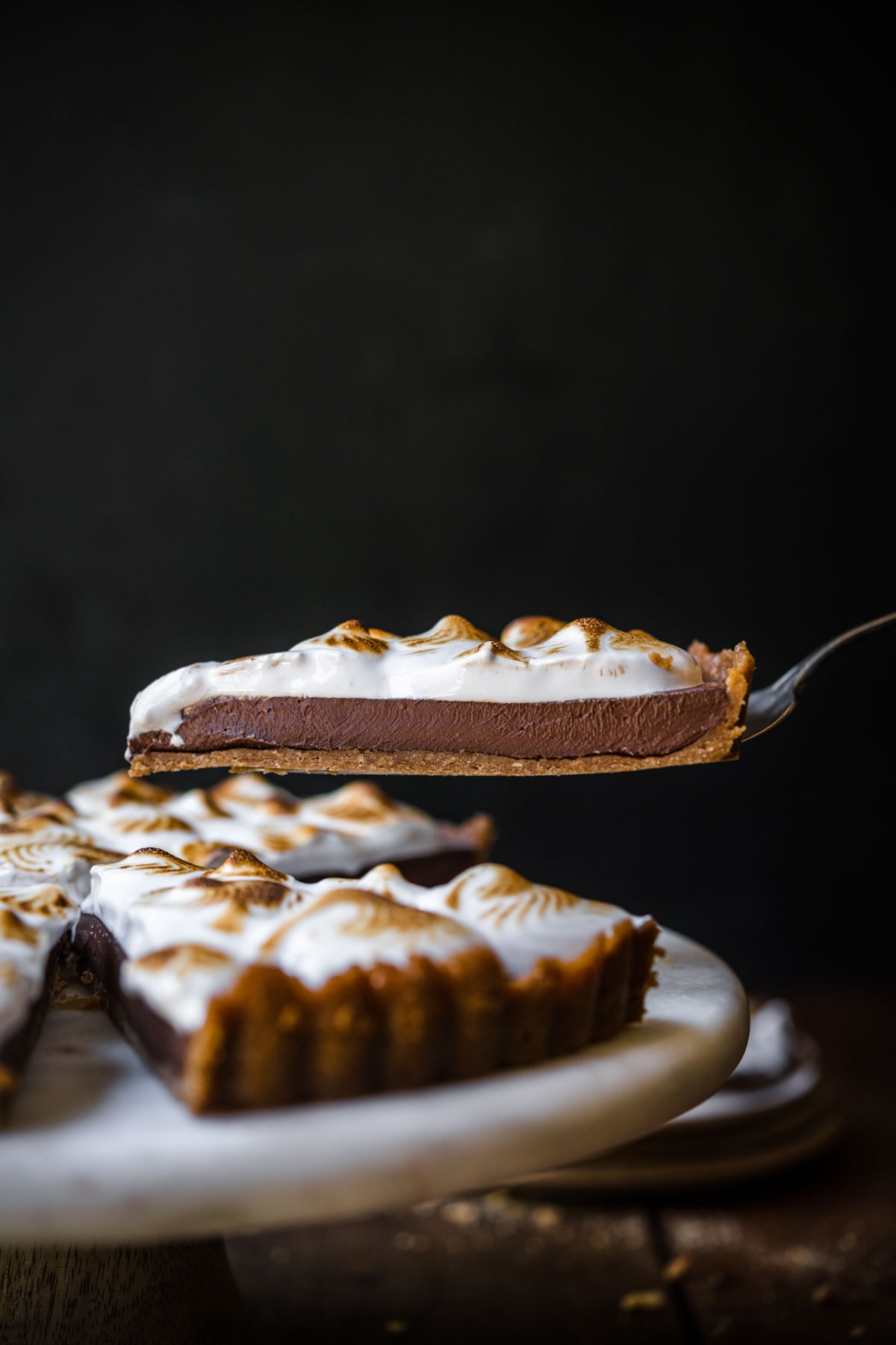 side view of person lifting up slice of vegan s'mores tart from cake stand. 