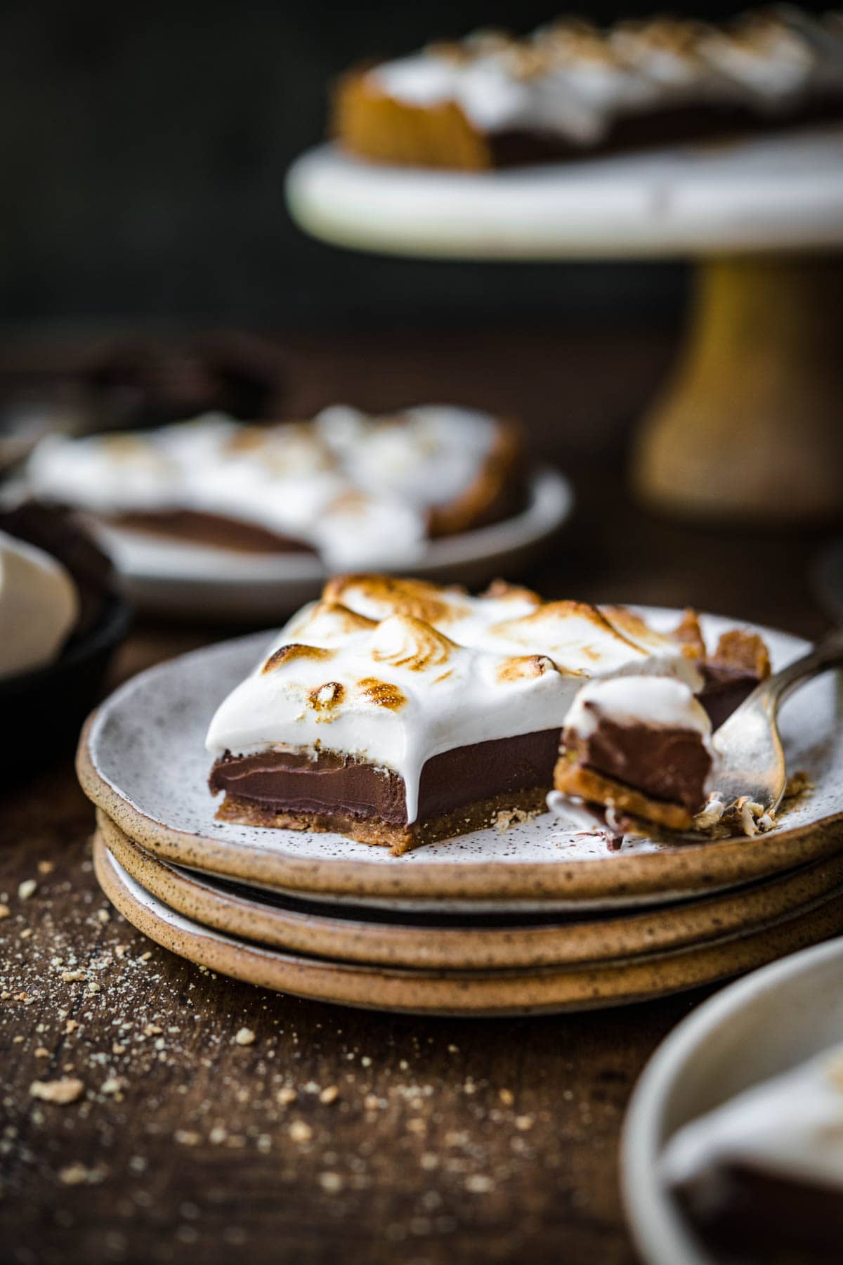 side view of slice of vegan s'mores tart on stack of plates on wood table. 