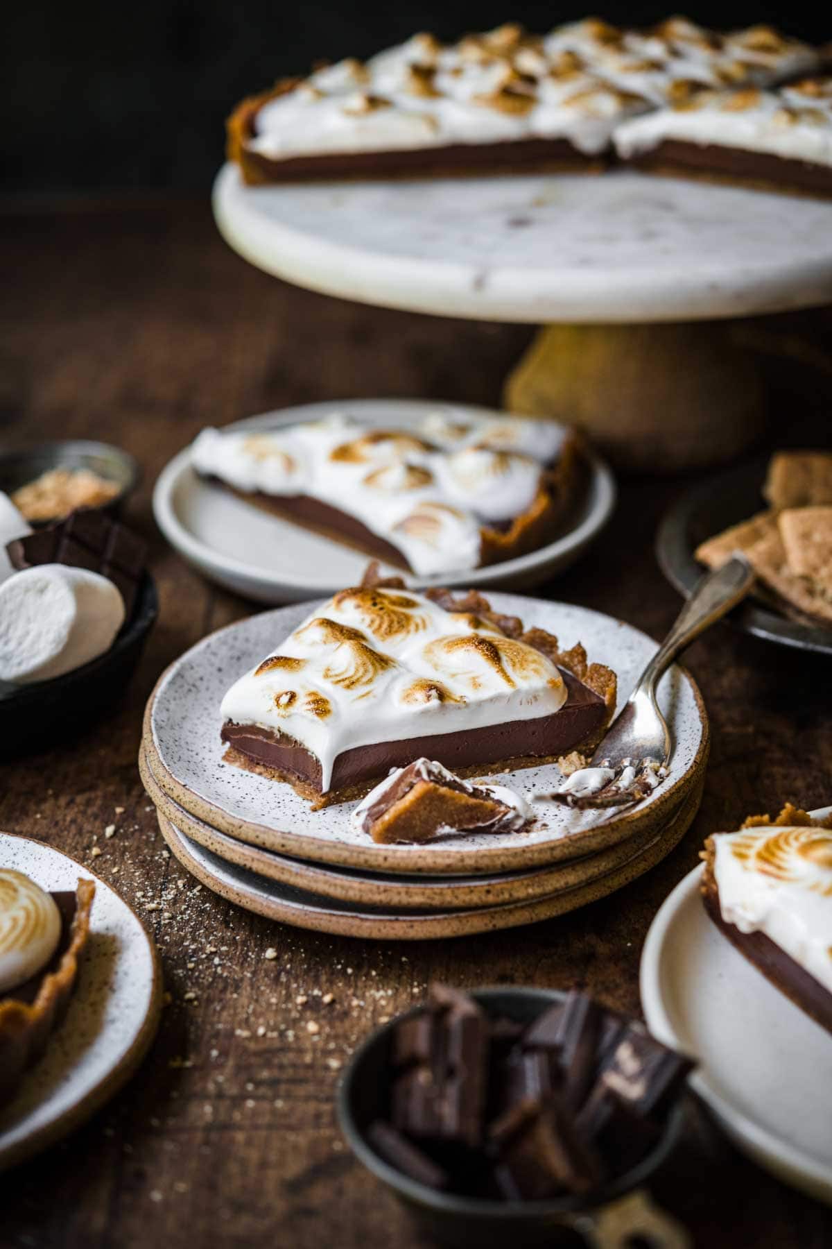 side view of slice of vegan s'mores tart on stack of plates on wood table. 