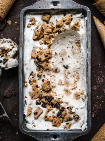 overhead view of vegan cookie dough ice cream in antique tin with ice cream cones around it.