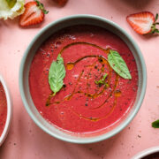 close up overhead view of strawberry watermelon gazpacho in light green bowl topped with fresh basil.