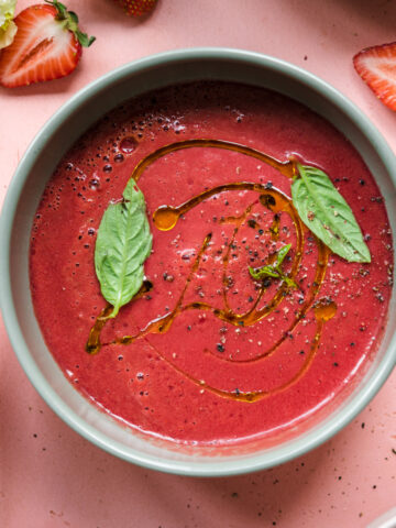 close up overhead view of strawberry watermelon gazpacho in light green bowl topped with fresh basil.