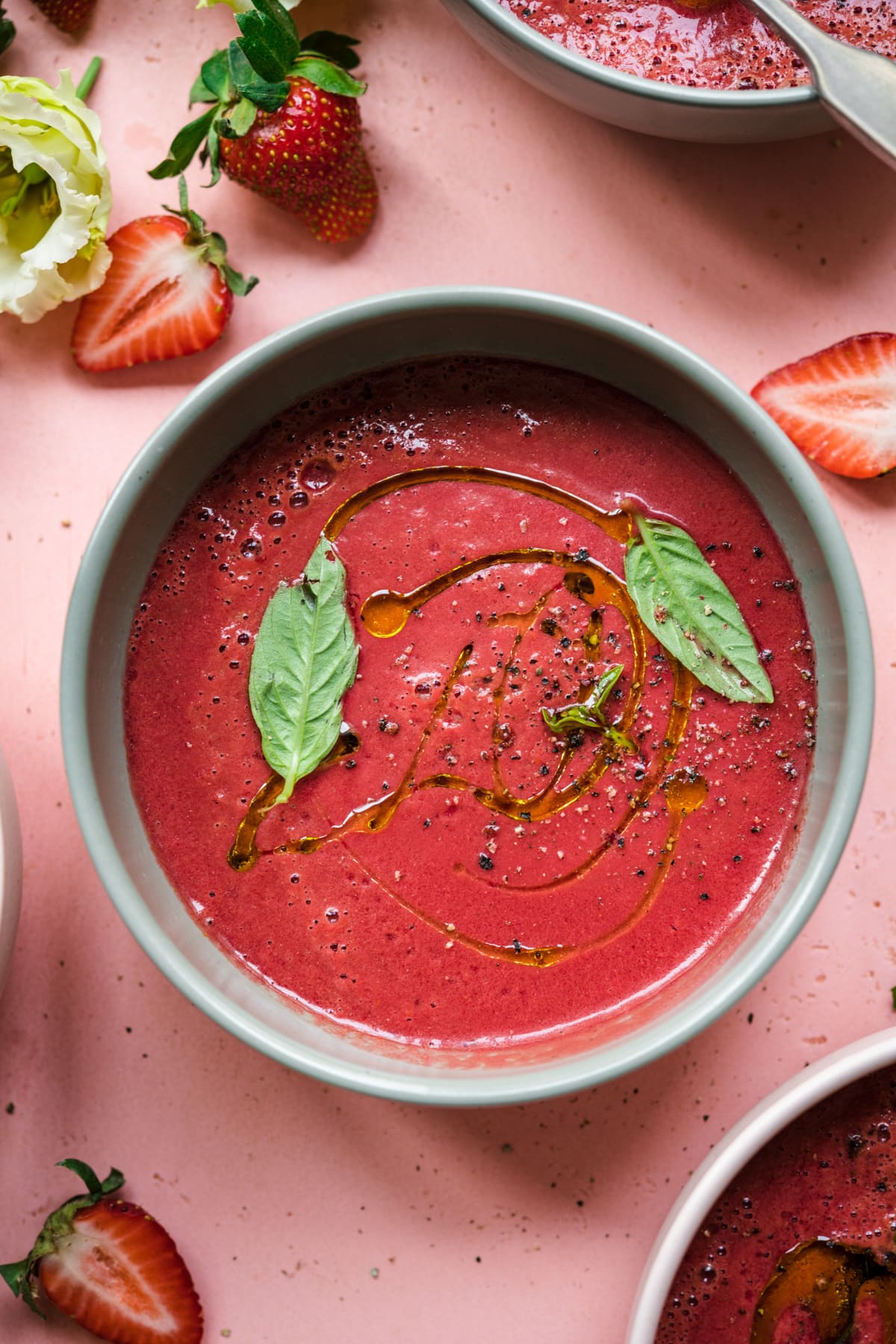 close up overhead view of strawberry watermelon gazpacho in light green bowl topped with fresh basil.
