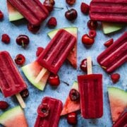 overhead view of watermelon berry popsicles with fresh fruit and ice on blue background.