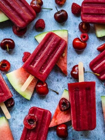 overhead view of watermelon berry popsicles with fresh fruit and ice on blue background.