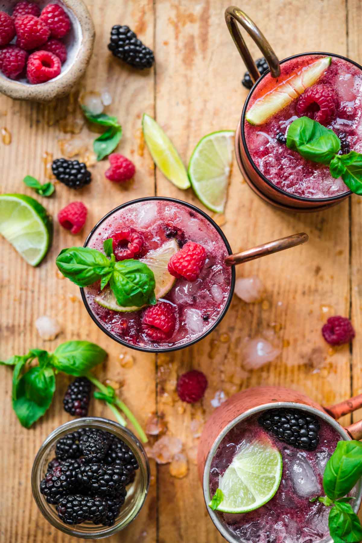 overhead view of berry basil moscow mules garnished with basil and raspberries on wood table. 