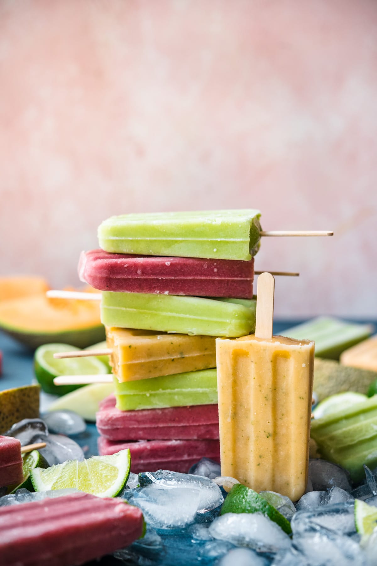 Stack of melon yogurt popsicles surrounded by crushed ice and fresh melons. 