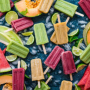 overhead view of watermelon, cantaloupe and honeydew melon yogurt popsicles on blue backdrop with fresh melon.