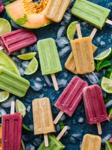 overhead view of watermelon, cantaloupe and honeydew melon yogurt popsicles on blue backdrop with fresh melon.