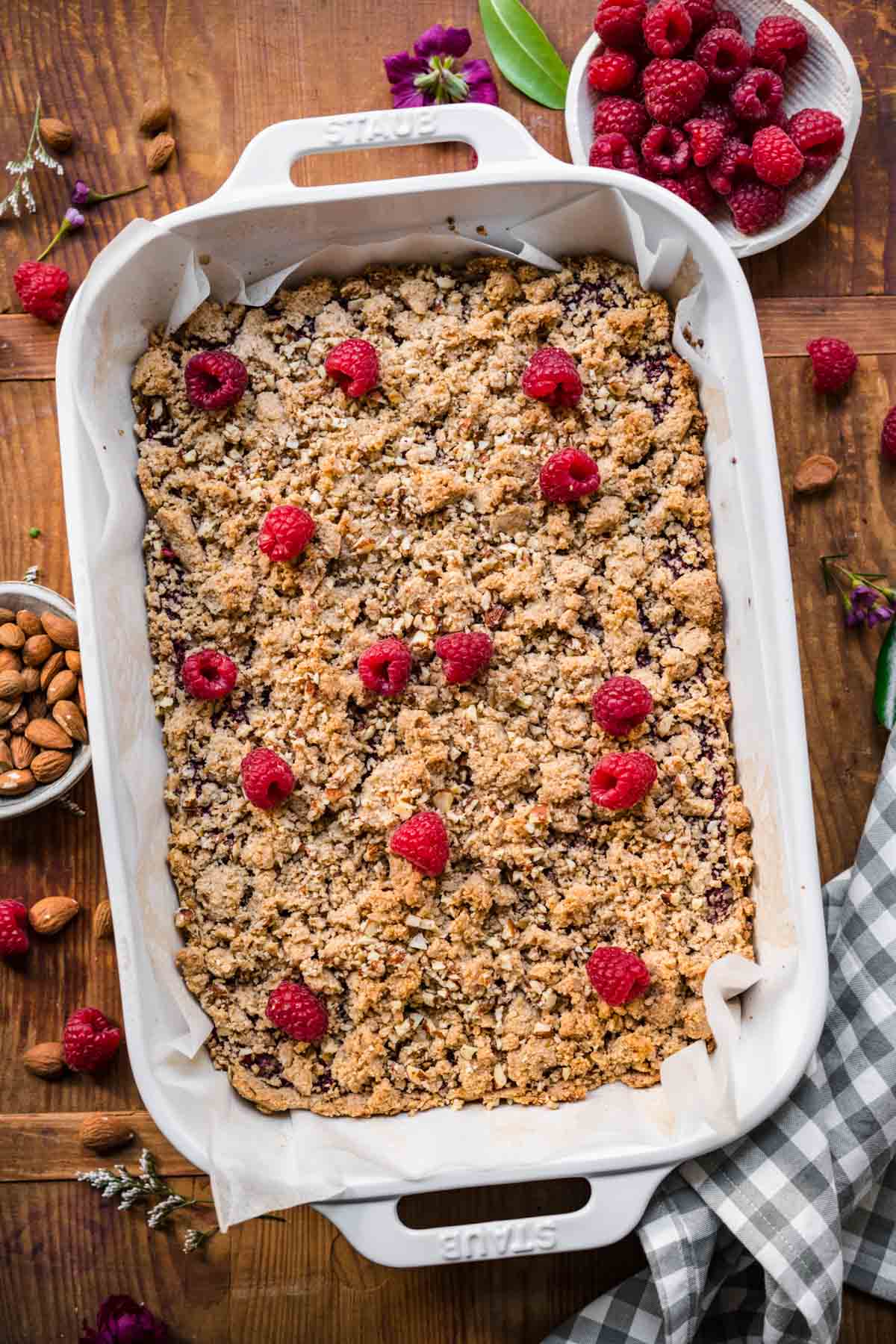 overhead view of raspberry crumble bars in white baking pan with fresh raspberries on top. 