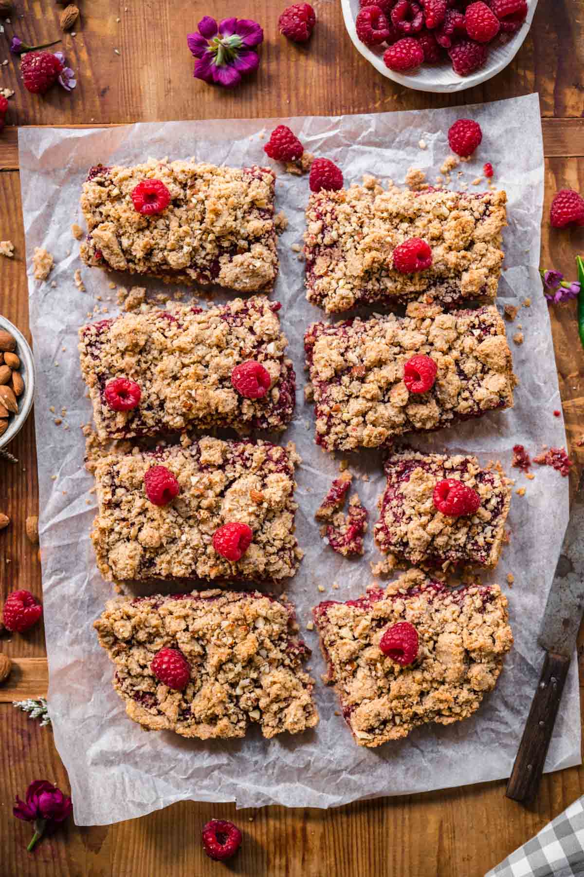 overhead view of sliced raspberry crumble bars on parchment paper with fresh raspberries. 