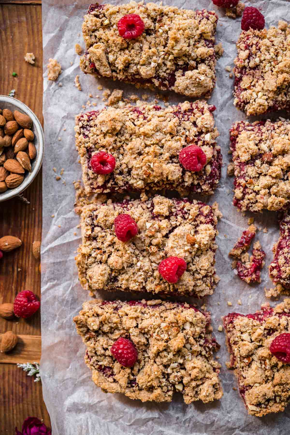 overhead view of sliced raspberry crumble bars on parchment paper with fresh raspberries. 