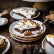 side view of slice of vegan s'mores tart on stack of plates on wood table.