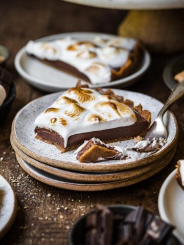 side view of slice of vegan s'mores tart on stack of plates on wood table.