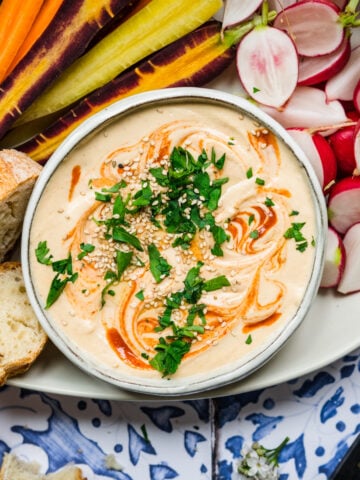 close up overhead view of sriracha white bean dip on a platter with fresh vegetables.