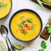 close up view of vegan corn chowder in a blue bowl topped with serrano pepper and cilantro.