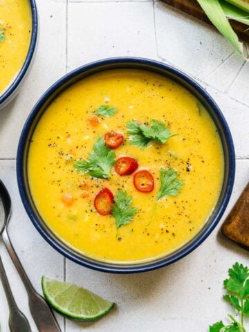 close up view of vegan corn chowder in a blue bowl topped with serrano pepper and cilantro.