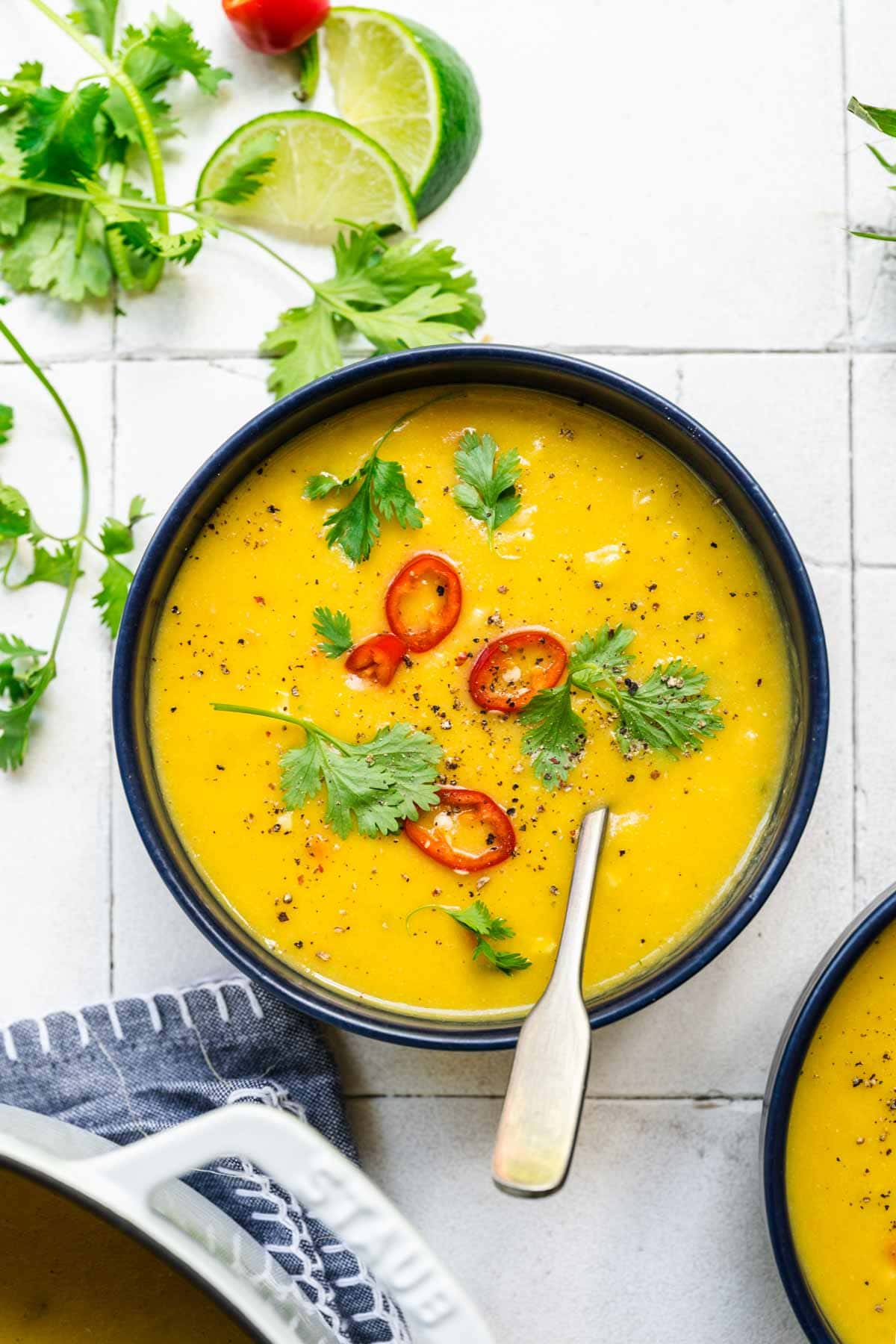 overhead view of vegan corn chowder in a blue bowl topped with serrano pepper and cilantro. 