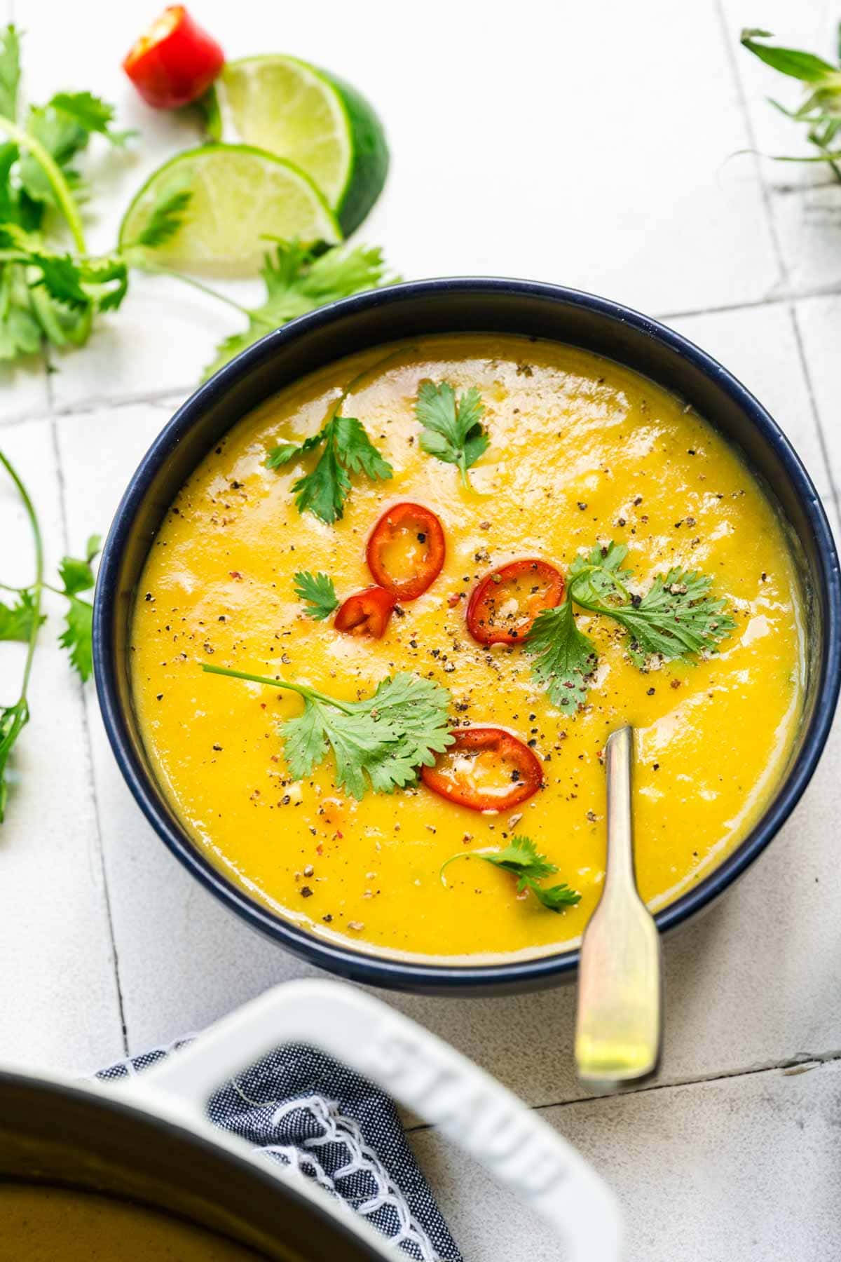 close up view of vegan corn chowder in a blue bowl topped with serrano pepper and cilantro. 