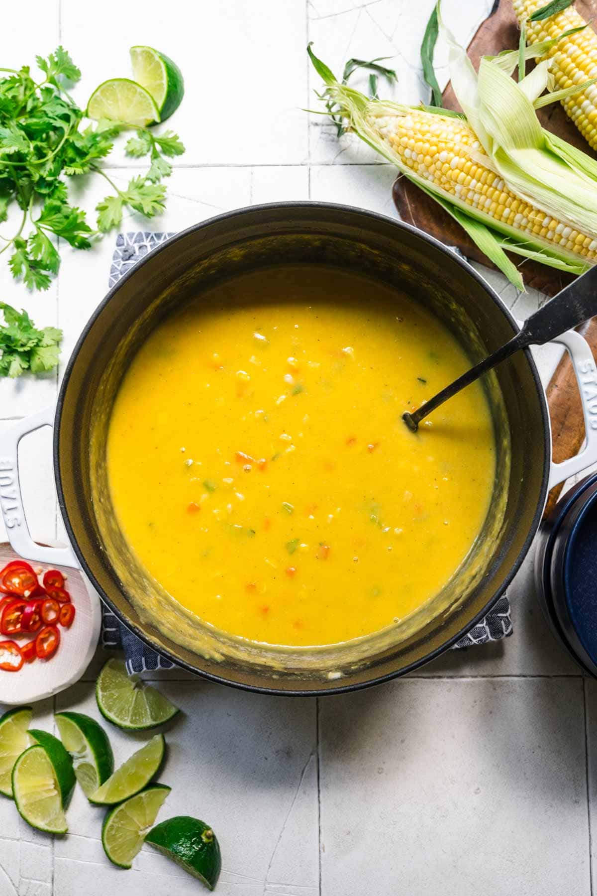 overhead view of vegan corn chowder in large soup pot on white tile background. 