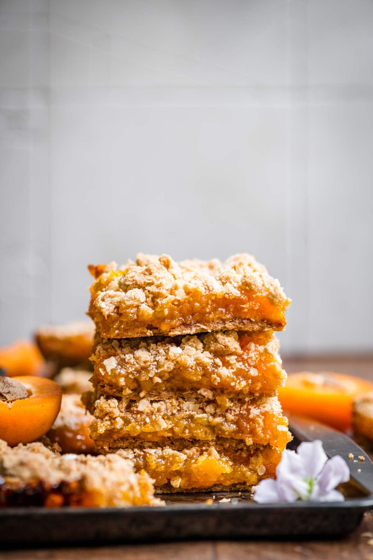 4 crumble bars stacked on top of one another with apricots spread throughout the background.