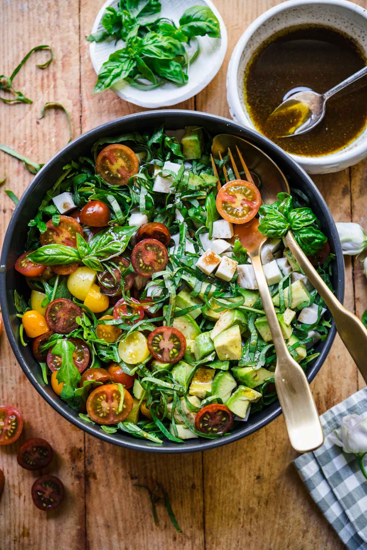 Overhead view of salad in a bowl with fork and a spoon, basil garnish, and dressing on the side.