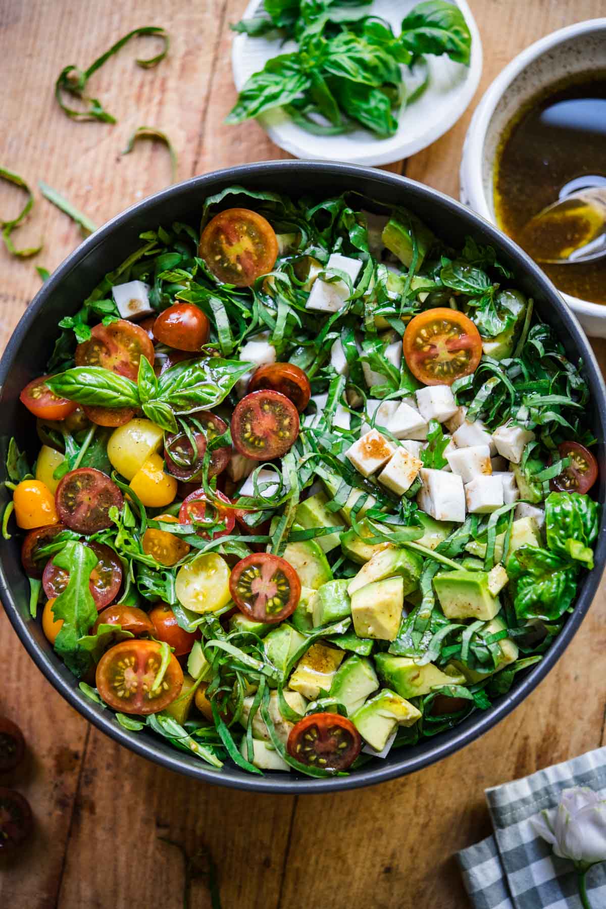 Overhead view of arugula caprese salad in a bowl with basil garnish, and dressing on the side.