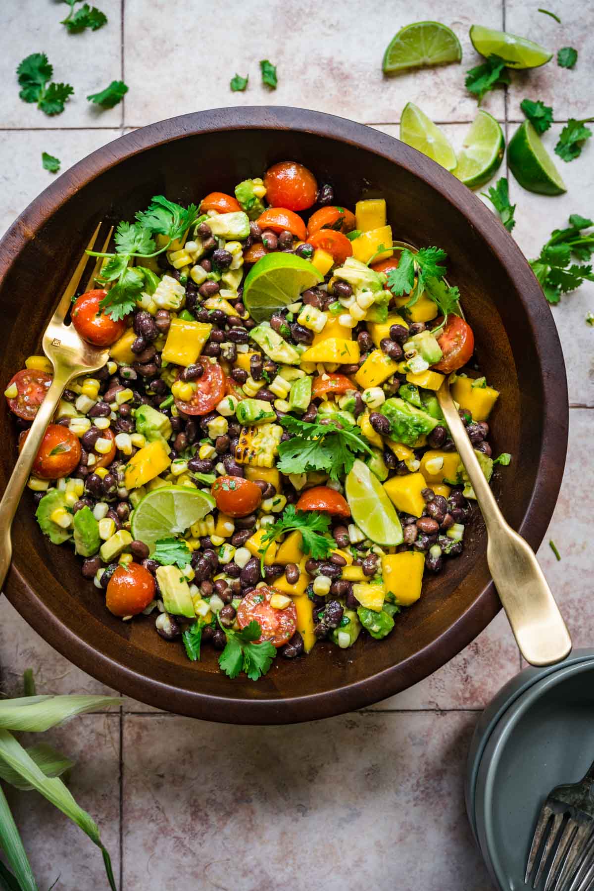 Black bean and mango salad seen from above in a wooden bowl with a fork and a spoon.