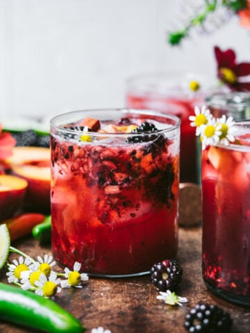 side view of blackberry peach cocktail with summer flowers.