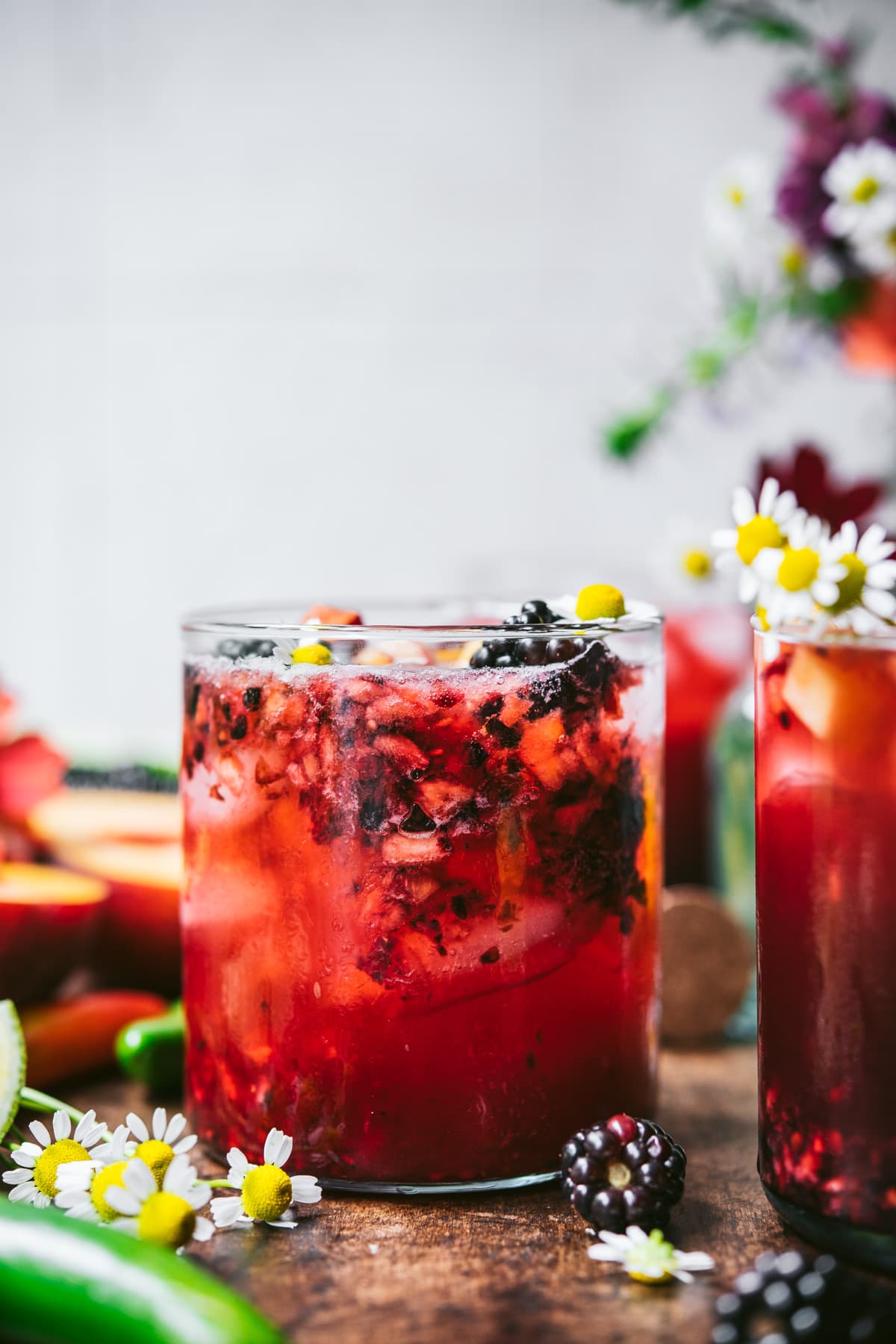side view of blackberry peach cocktail with summer flowers. 