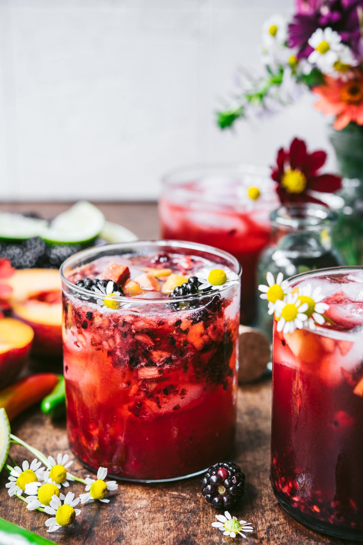 side view of blackberry peach cocktail with summer flowers. 