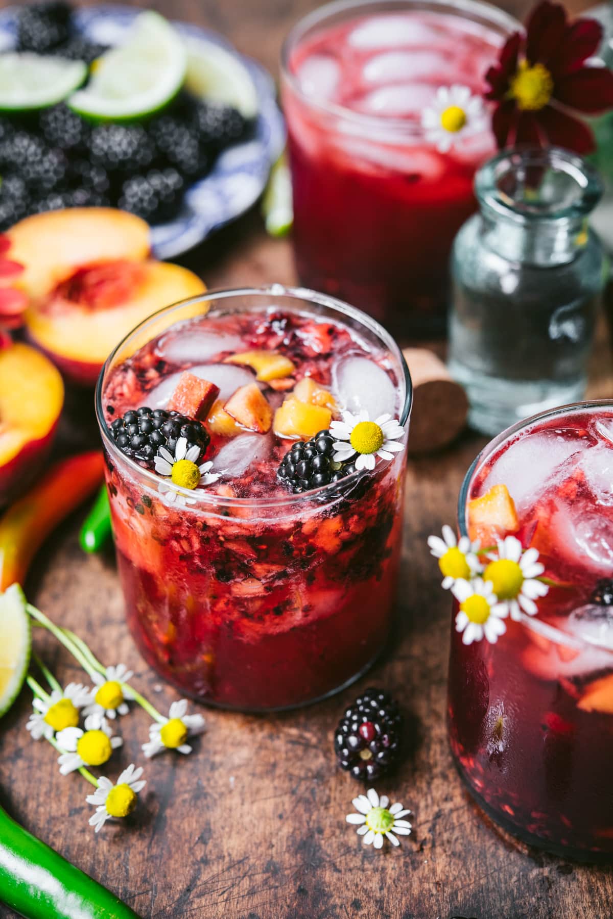 side view of blackberry peach cocktail with summer flowers. 