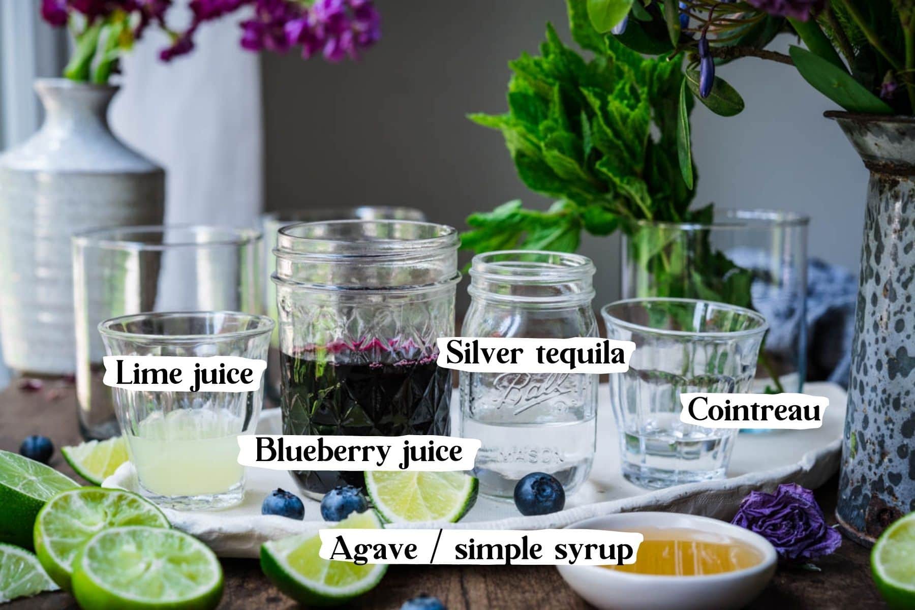 Front view of cocktail ingredients, including lime juice, blueberry juice, silver tequila, cointreau, and agave.