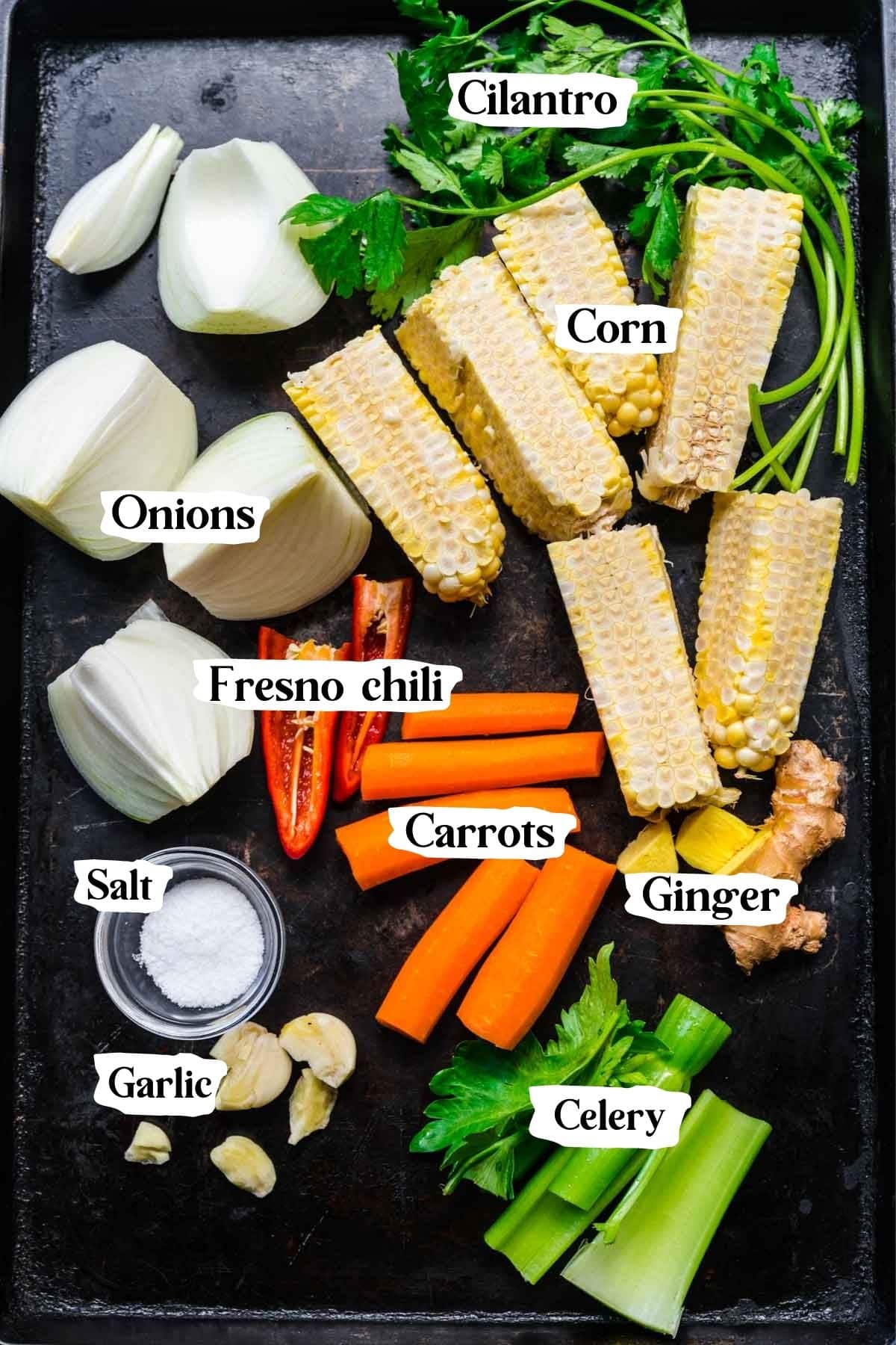 Overhead shot of corn stock ingredients, including corn cobs, onions, fresno chilis, carrots, etc.