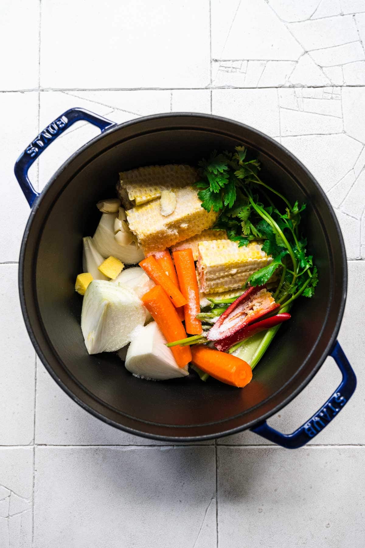 Pot full of corn stock ingredients, including corn, onions, parsley, and peppers.