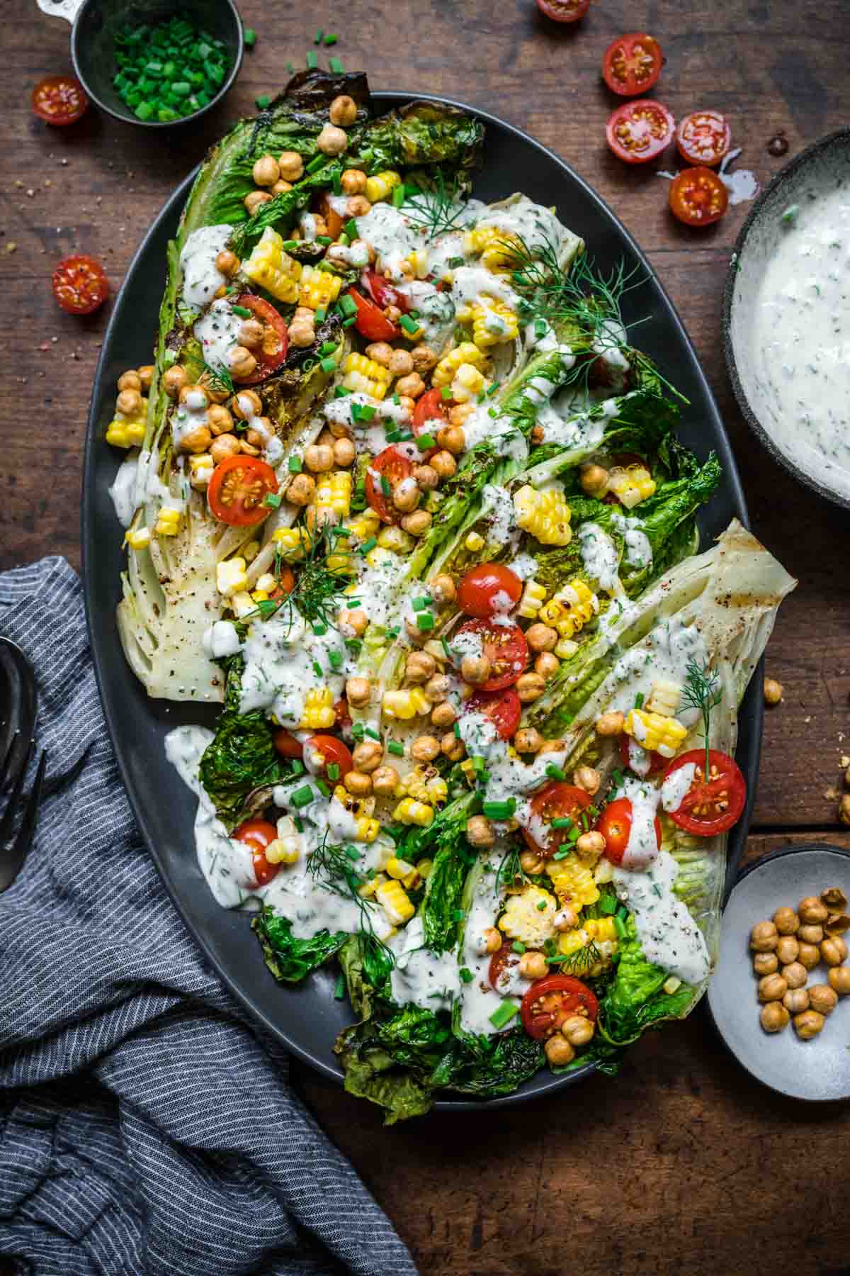 Overhead view of 4 heads of grilled romaine with crispy chickpeas, corn, tomatoes, and vegan ranch.